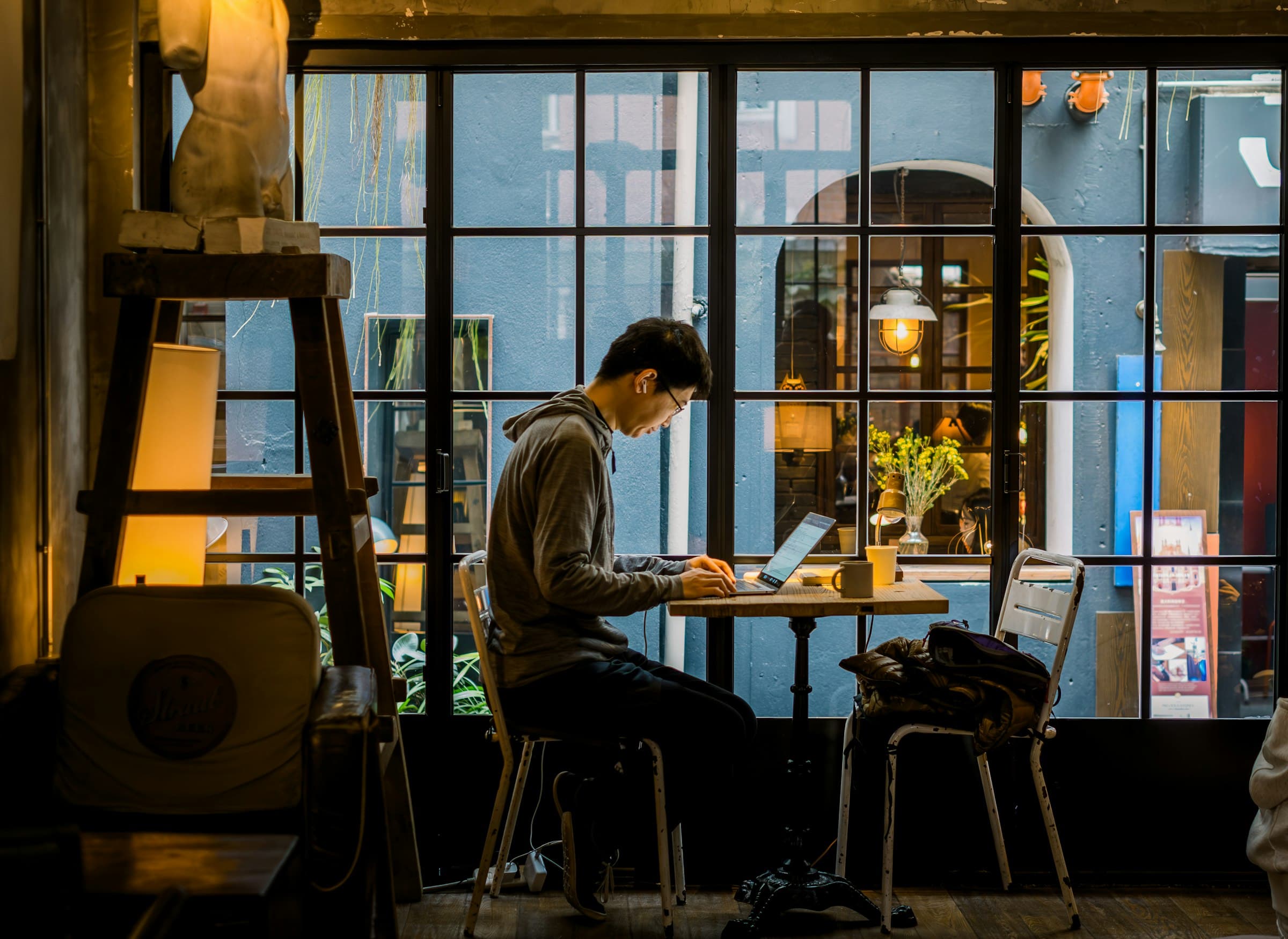 Homem jovem trabalhando no notebook à janela de um café