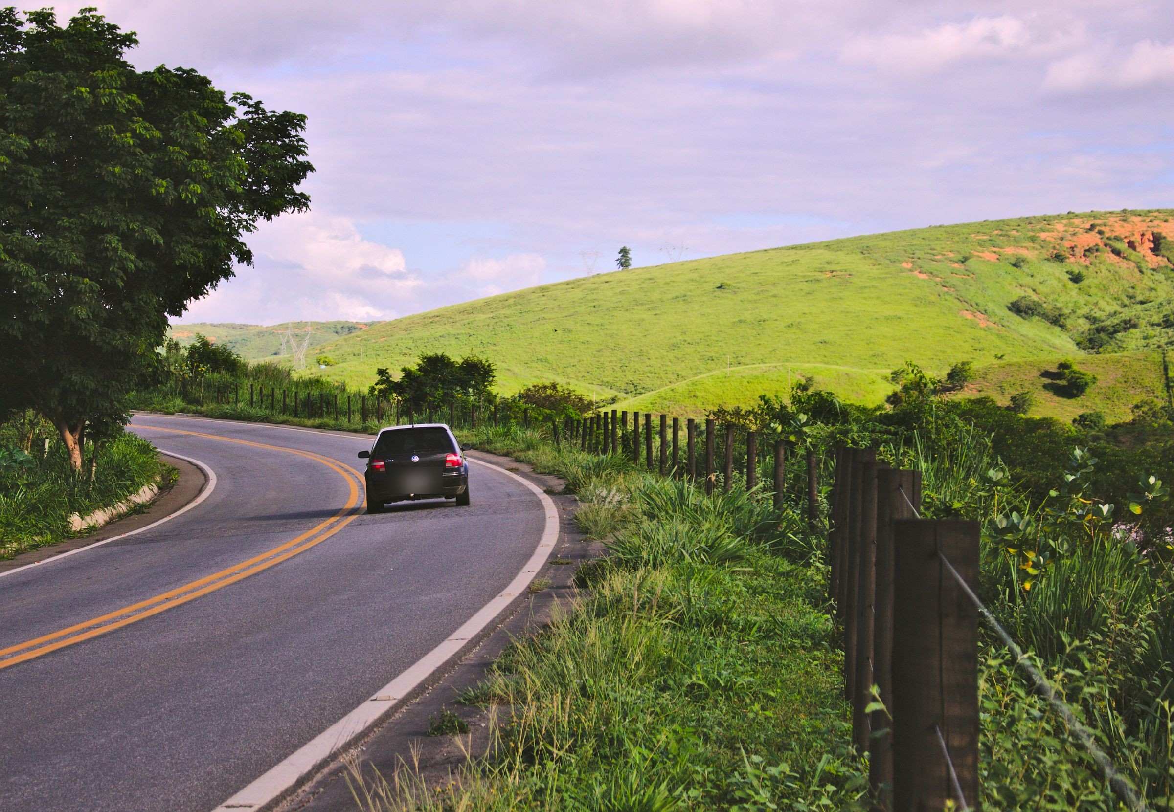 Carro em estrada de pista dupla cortando paisagem verde brasileira, no fim de tarde