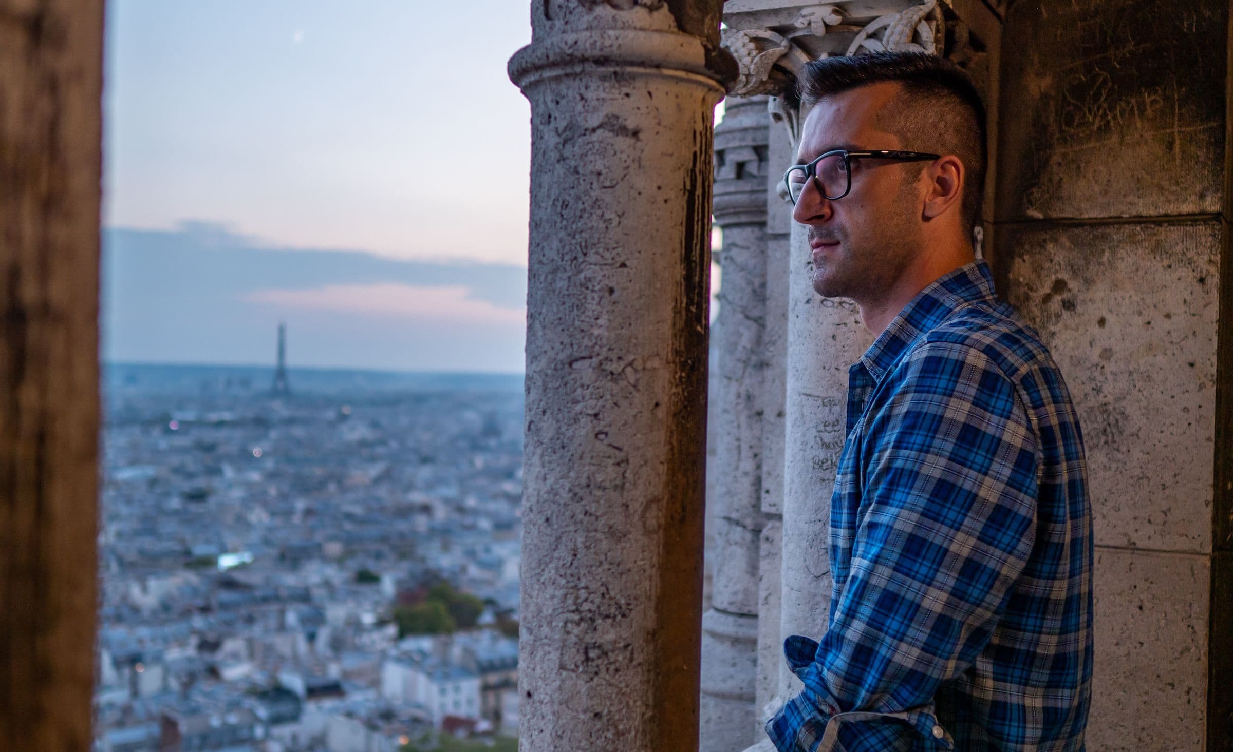 Viajante observando o horizonte de Paris e a Torre Eiffel ao entardecer, do alto de um mirante histórico.